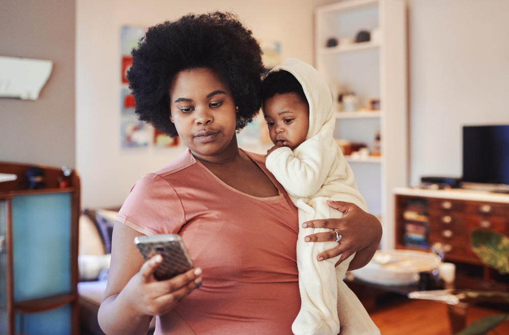 A woman holding a baby in one arm and texting on a phone in her other hand